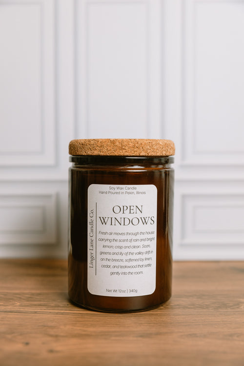 Dark amber colored recycled glass Candle jar labeled 'Open Windows' with a cork lid on a wooden surface.