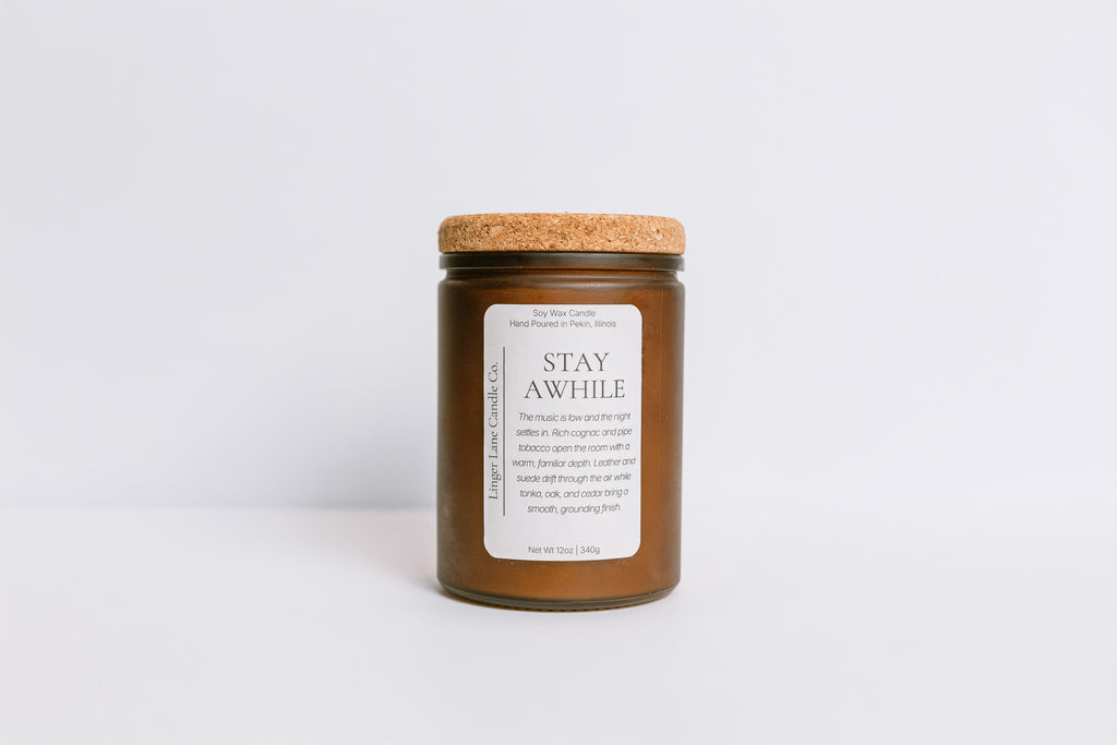 Frosted brown recycled glass Candle jar with cork lid and 'Stay Awhile' label on a white background