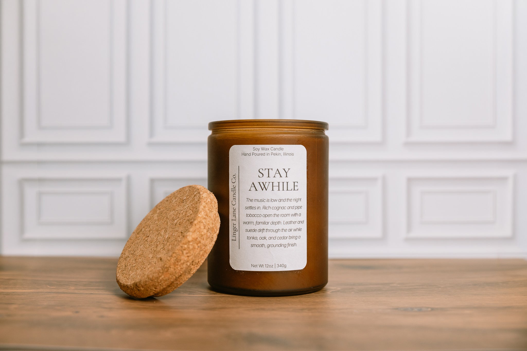 Scented soy wax Candle with a cork lid and 'Stay Awhile' label on a wooden surface.