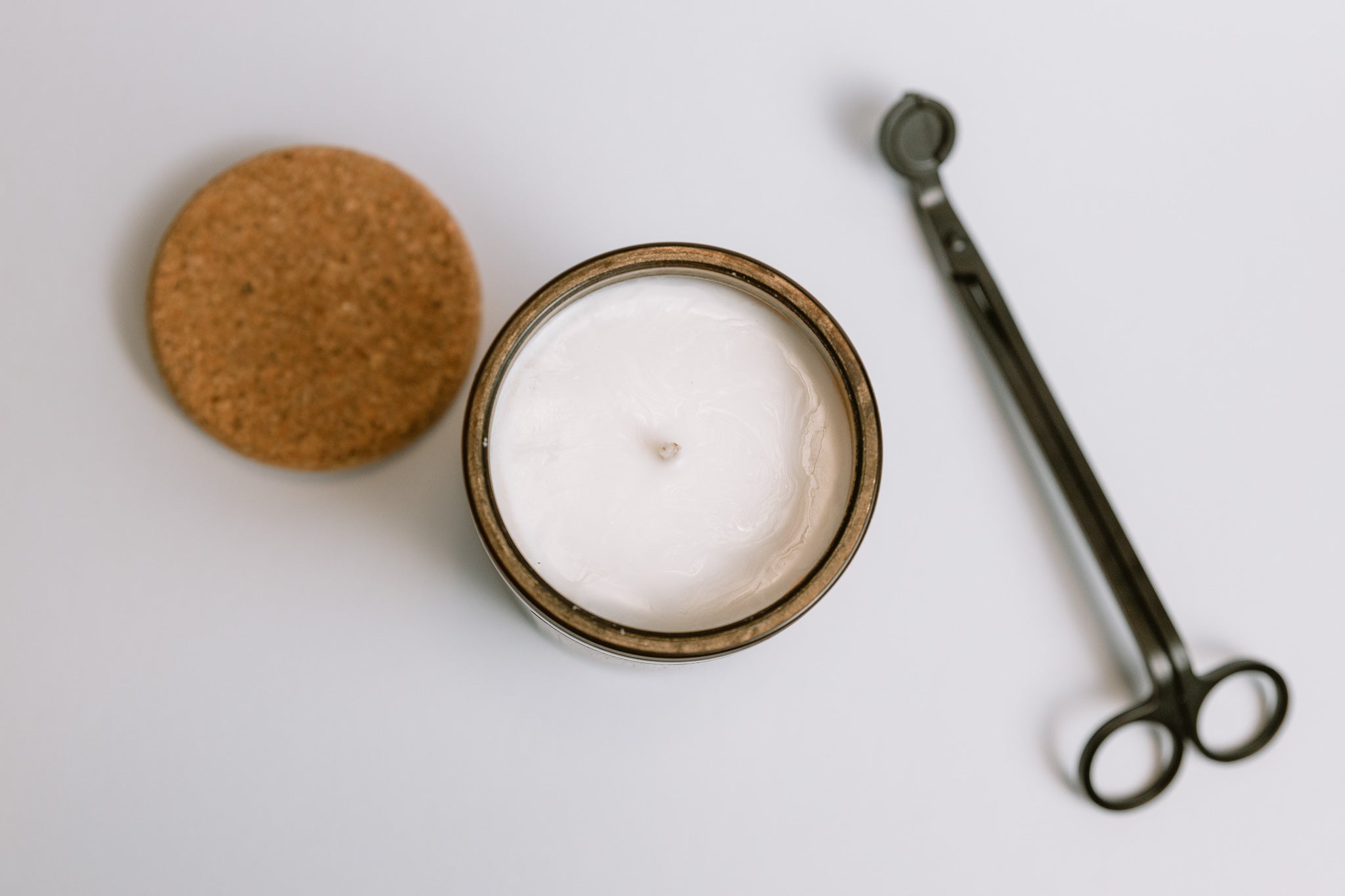 Hand poured soy wax candle in a glass jar with a cork lid and wick trimmer on a white background