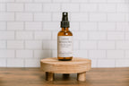Bottle of 'Open Windows' scented room spray on a wooden stand with a white tiled wall background