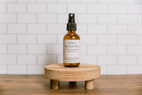 Bottle of 'Open Windows' scented room spray on a wooden stand with a white tiled wall background