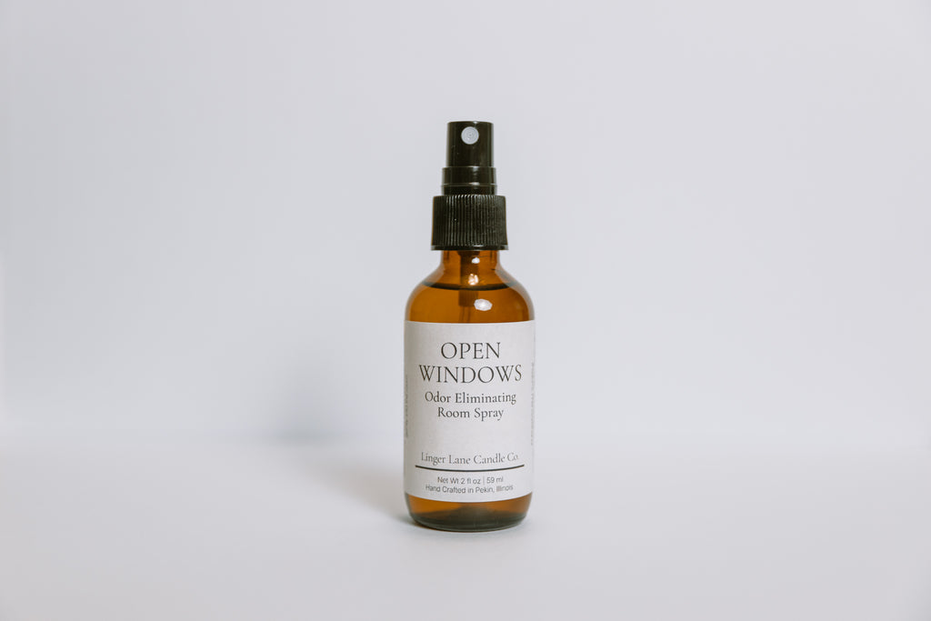 Scented odor eliminating room spray in an amber bottle labeled 'Open Windows' on a white background
