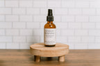 Bottle of 'Sunday Morning' odor eliminating room spray on a wooden stand with a tiled wall background