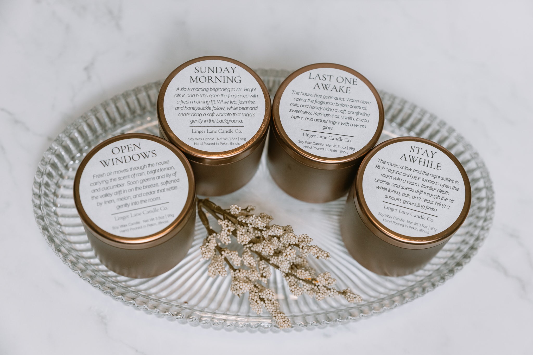 Four candles with labels on a glass tray on a marble surface