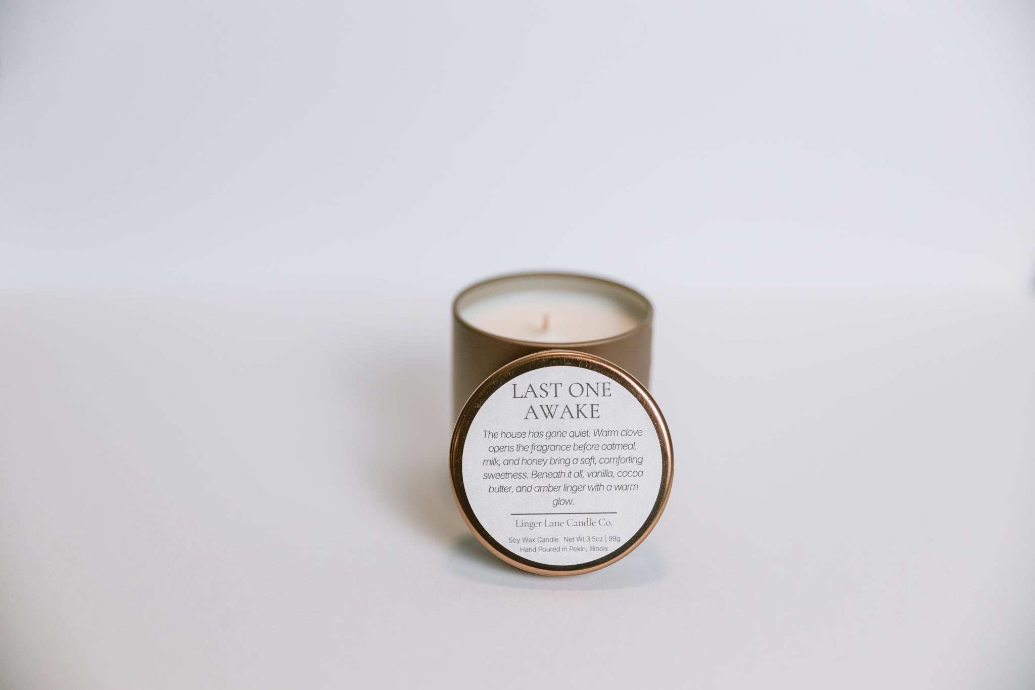 Candle labeled 'Last One Awake' in a bronze tin on a white background