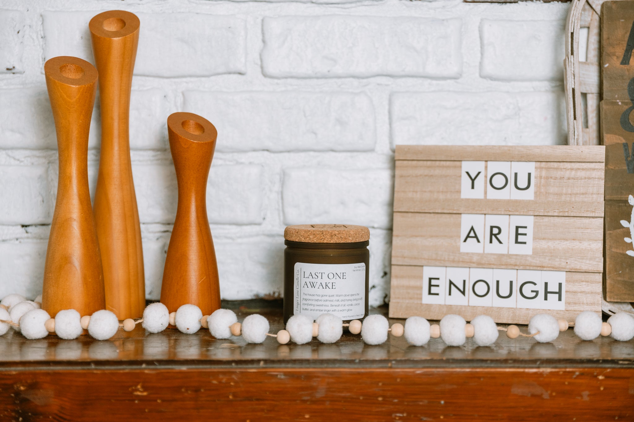 Decorative shelf with wooden vases, a candle, and a sign saying 'You are enough' against a white brick wall.