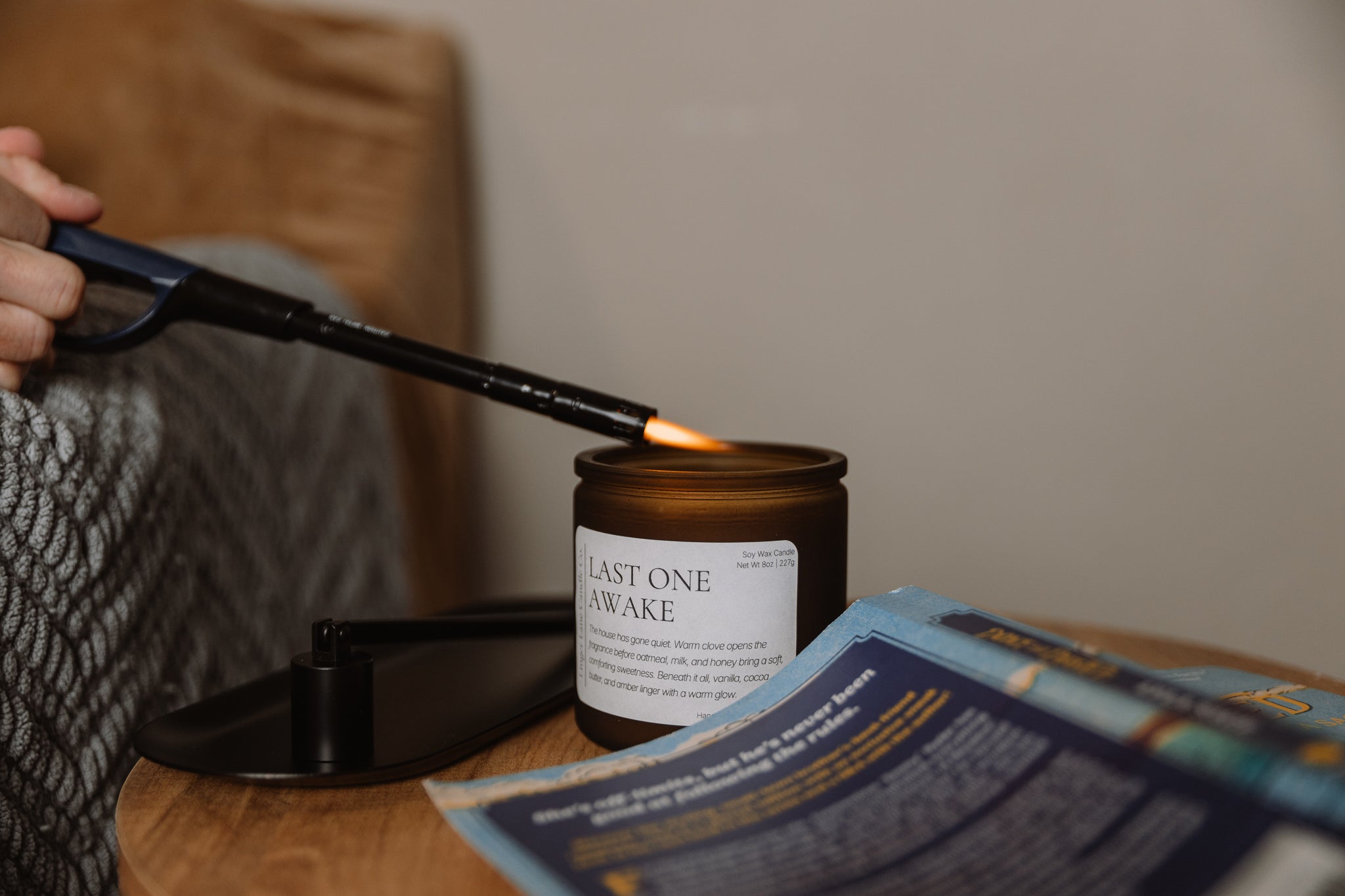 Person lighting a candle labeled 'Last One Awake' with a lighter, on a wooden surface.