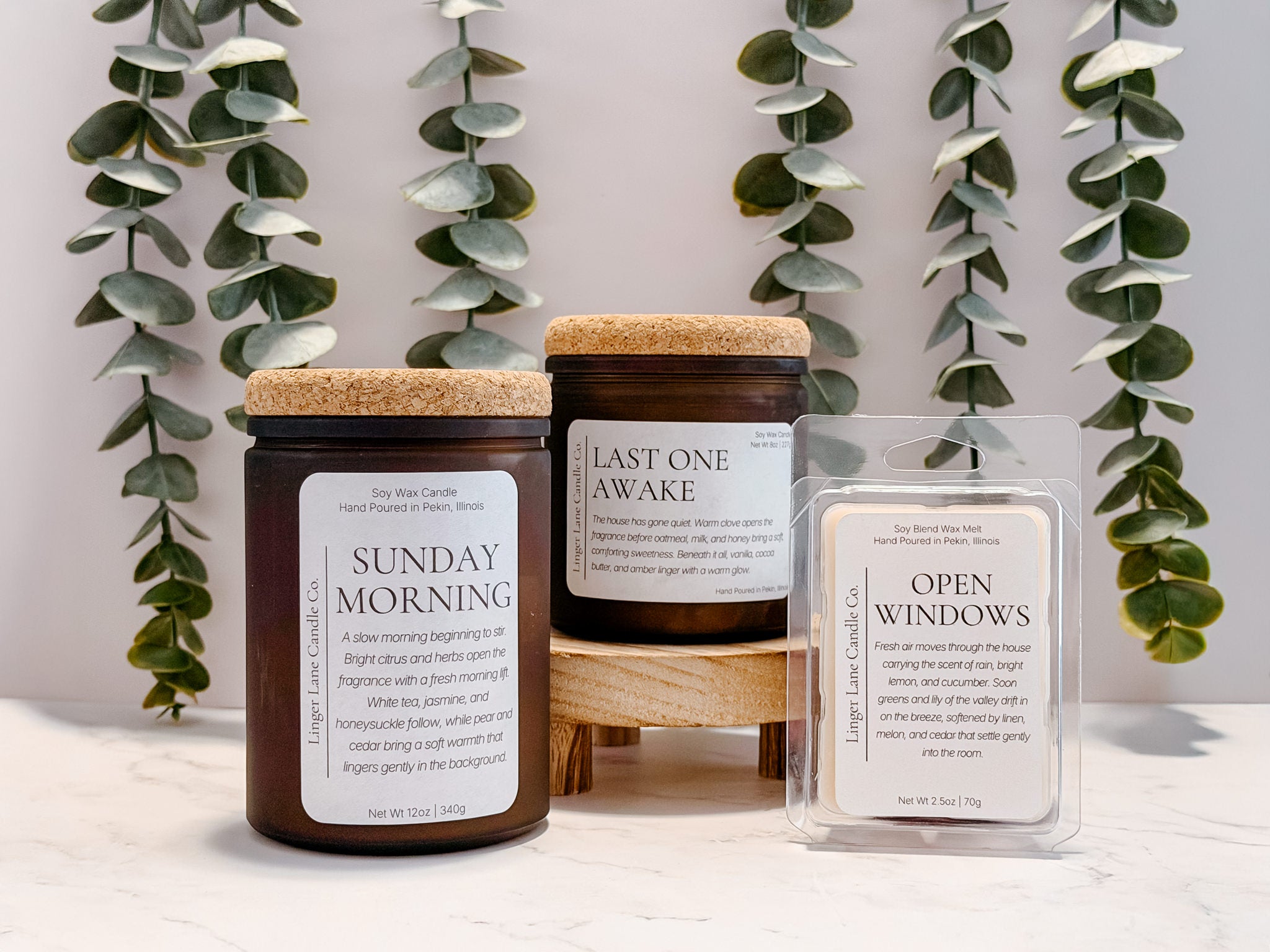 Two soy candles and a wax melt on a surface with greenery in the background