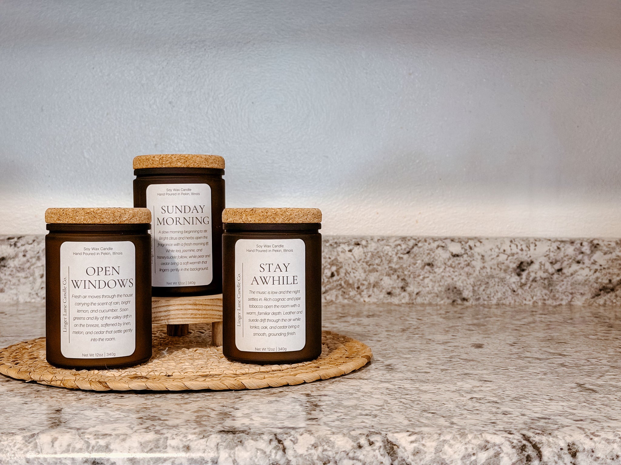 Three candles with labels on a woven mat against a neutral background