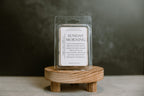Packaged wax melt labeled 'Sunday Morning' on a wooden stand with a dark background