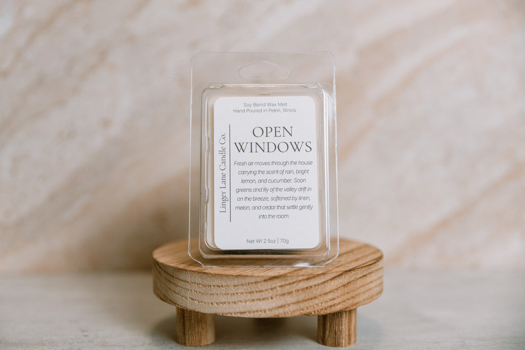 Candle wax melt packaging labeled 'Open Windows' on a wooden stand with a neutral background
