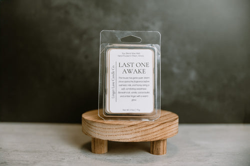 Wax melt package labeled 'Last One Awake' on a wooden stand with a dark background