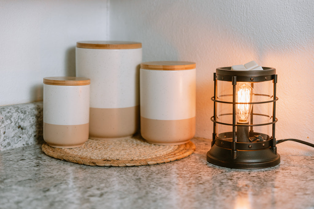 Set of ceramic jars with wooden lids on a textured surface next to a vintage-style lantern wax warmer.