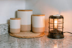 Set of ceramic jars with wooden lids on a textured surface next to a vintage-style lantern wax warmer.